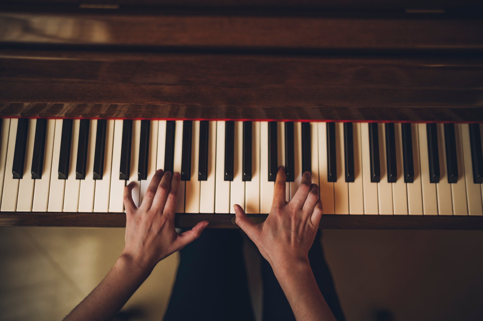 Hands of a person playing his wooden upright piano