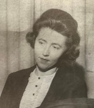 Black and white vintage portrait photograph of a woman wearing a dark blazer over a light blouse, with styled dark hair, looking toward the camera